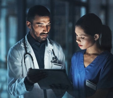 Photo of doctor and nurse standing in hallway while looking at a tablet.