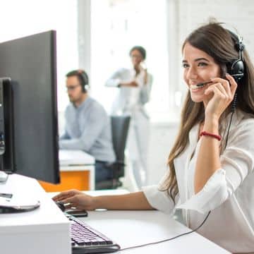 A woman with a phone headset using a desktop computer as part of a managed it services team