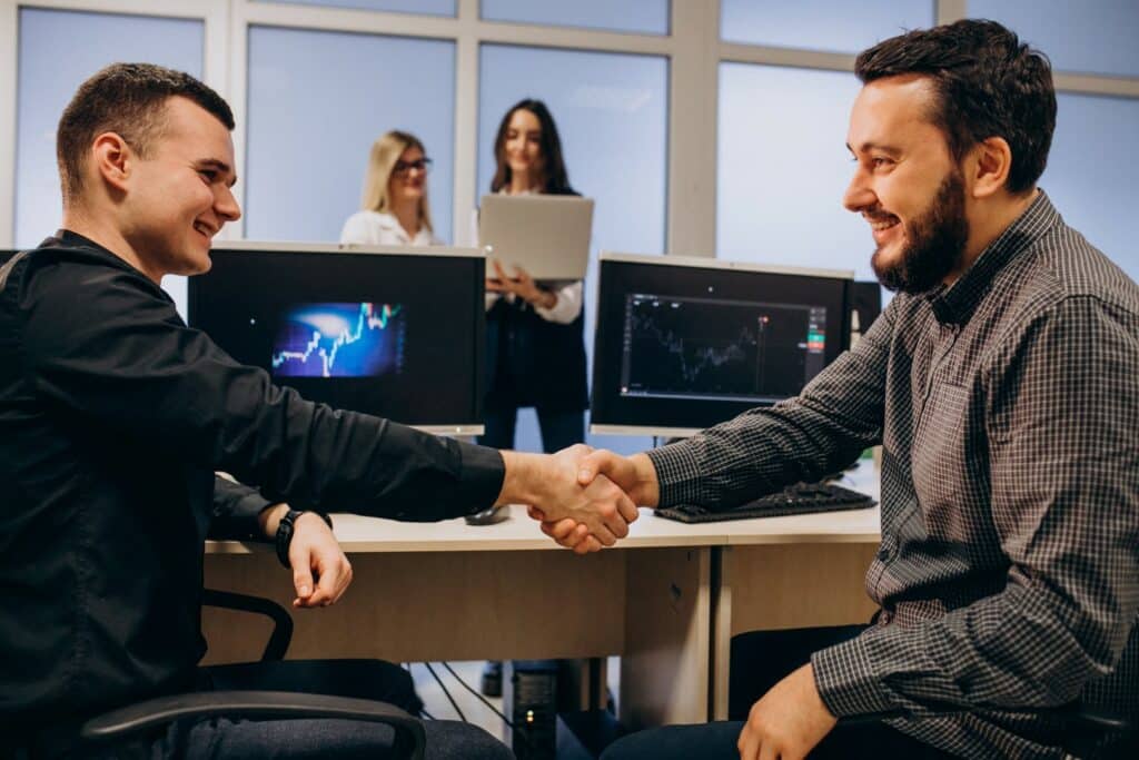 two men sitting at computers shaking hands